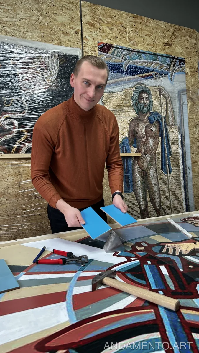 Мастер создает мозаику мотоциклист в мастерской, держа в руках синие плитки.